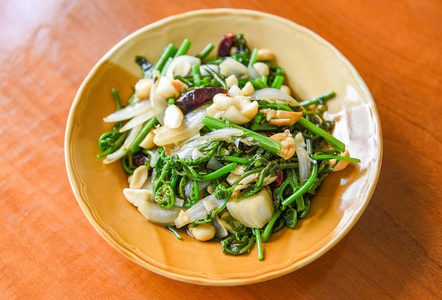 Verdure fritte - Mescolare la felce paco con noci di macadamia in cima sul piatto bianco