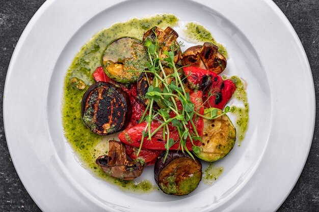 Verdure grigliate al forno tritate con funghi, zucchine, melanzane, peperoni, funghi, su una piastra bianca con salsa