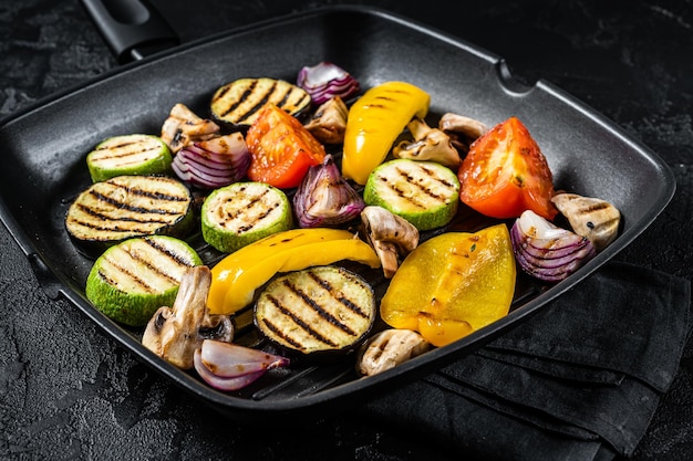 Verdure grigliate in una padella grill peperone zucchine melanzane cipolla e pomodoro Sfondo nero Vista dall'alto