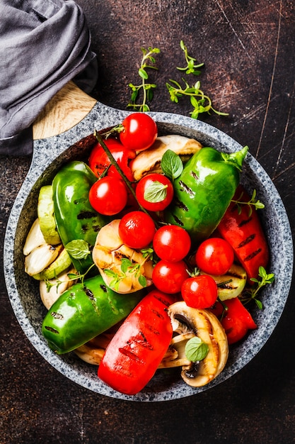 Verdure grigliate (peperoni, zucchine, funghi e pomodori in padella, sfondo scuro.