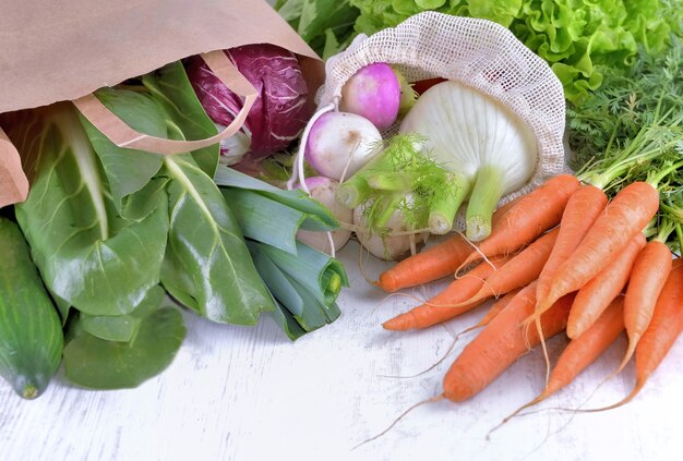 Verdure in sacchetti di carta e riutilizzabili tra le altre verdure fresche su un tavolo bianco