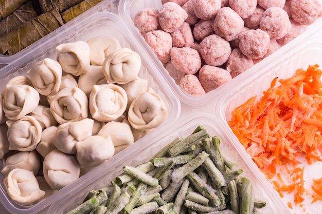 Verdure surgelate e prodotti a base di carne semilavorati in contenitori di plastica su un piatto bianco. polpette, canederli, fagioli tritati e carote grattugiate