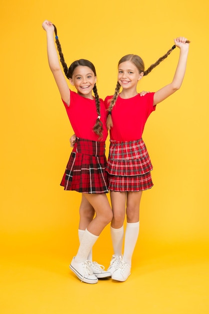 Veri amici. Piccole ragazze felici che indossano gli stessi abiti. Amici che godono dell'amicizia. Amici allegri. Felici insieme. Le ragazze della scuola si divertono insieme. Bambine sveglie sorridente sfondo giallo.