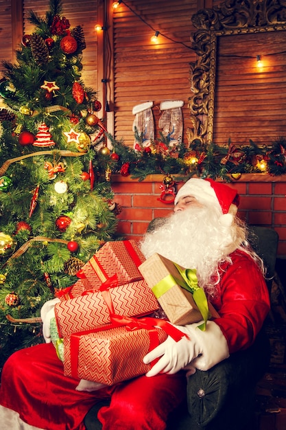 Vero Babbo Natale. Babbo Natale che dorme nel soggiorno vicino all'albero di Natale con i regali