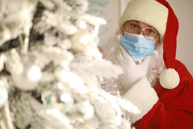 Vero Babbo Natale e albero di Natale su uno sfondo, con indosso una maschera protettiva, occhiali e cappello. Natale con distanza sociale. Covid-19
