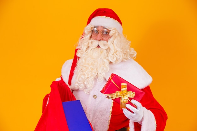 Vero Babbo Natale su sfondo giallo con borsa con vari regali di Natale.