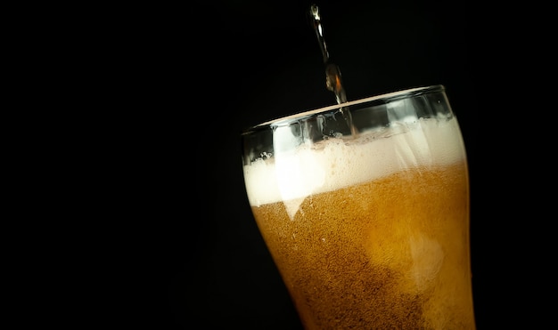 versa la birra in un bicchiere su uno sfondo scuro