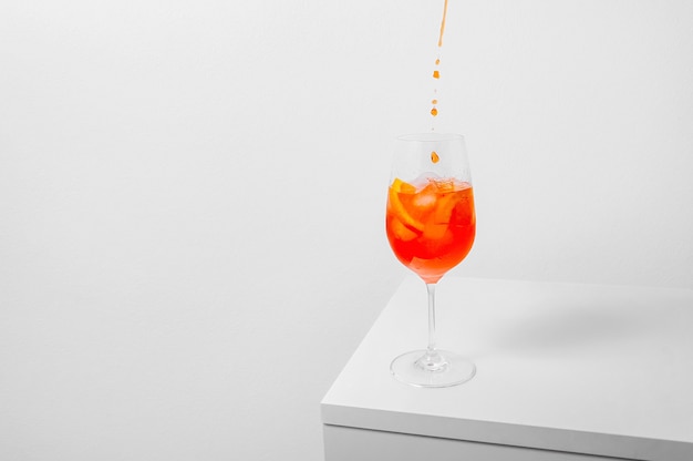 Versando aperol nel bicchiere di vino con ghiaccio su sfondo bianco