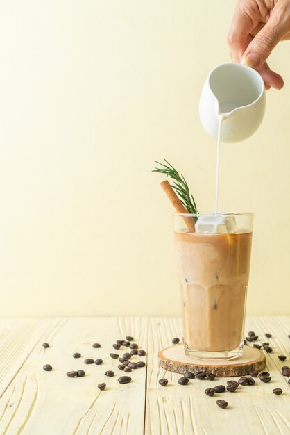 versando il latte nel bicchiere di caffè nero con cubetto di ghiaccio, cannella e rosmarino