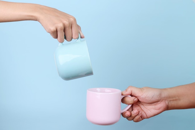 Versare a mano l'acqua da una tazza blu a una tazza rosa per il modello isolato su sfondo blu