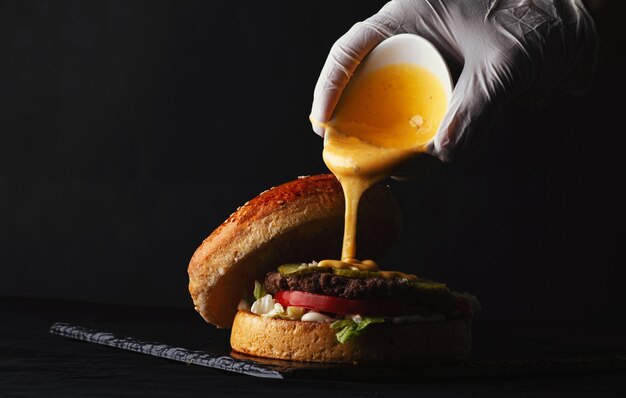 Versare a mano la salsa di formaggio fuso su Hamburger di manzo fatto in casa su piatto nero