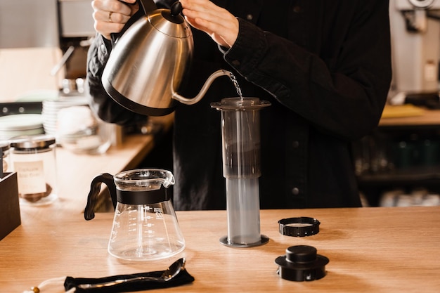 Versare acqua calda sui chicchi di caffè tostati e macinati in aeropress Processo di aeropress metodo alternativo di preparazione del caffè Il barista sta preparando il caffè aeropress nella caffetteria