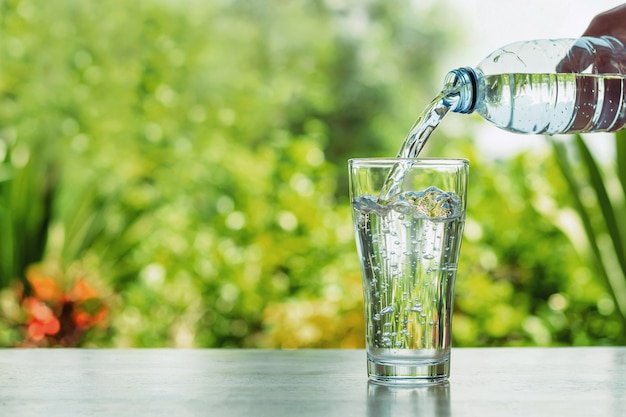 Versare acqua dalla bottiglia al bicchiere sullo sfondo della natura bokhek