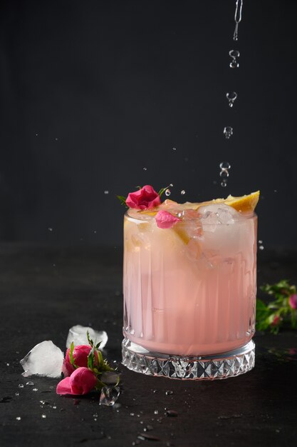 Versare cocktail alcolico rosa con fiori di rosa su sfondo nero