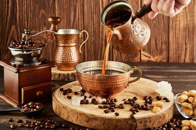 Versare il caffè dalla macchina da caffè in una tazza di rame un macinino da caffè antico e una brocca di latte di rame su