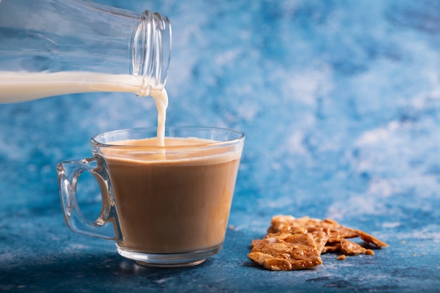 Versare il latte al caffè su sfondo blu