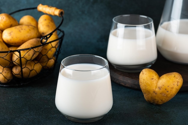 Versare il latte di patate vegano in vetro e patate in una ciotola su fondo scuro Latte vegano Latte vegetale sostitutivo del latte e senza lattosio Latte vegetale