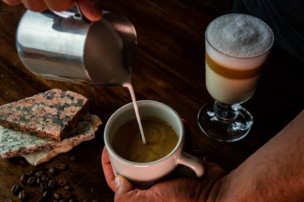 Versare il latte in una tazza con il caffè e un bicchiere con la schiuma