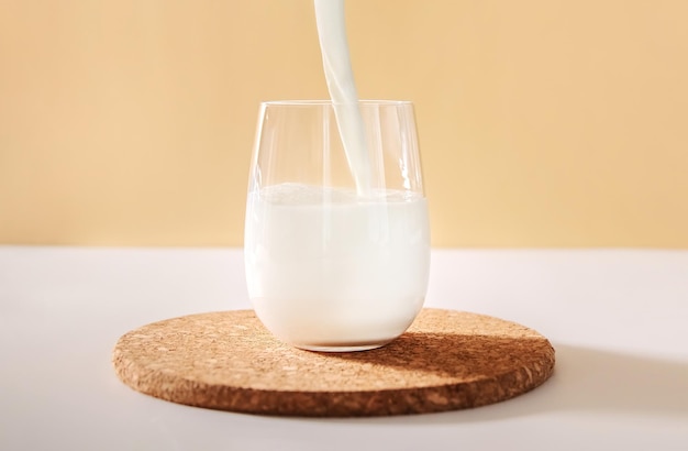 Versare il latte nel bicchiere su uno sfondo neutro chiaro