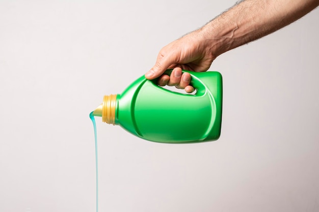 Versare il liquido detergente dalla bottiglia verde davanti a uno sfondo grigio chiaro, modello di serie mock-up modificabile pronto per il tuo design, percorso di selezione dell'etichetta incluso.