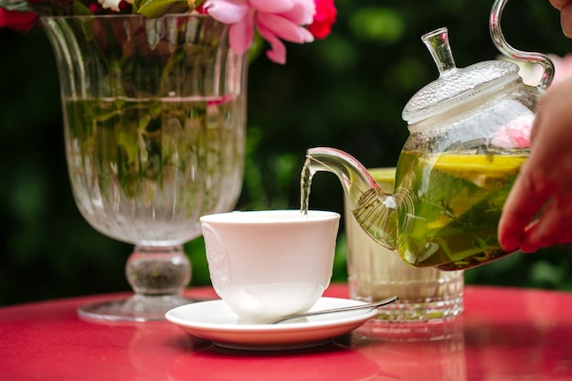 Versare il tè verde da una teiera di vetro in una tazza bianca