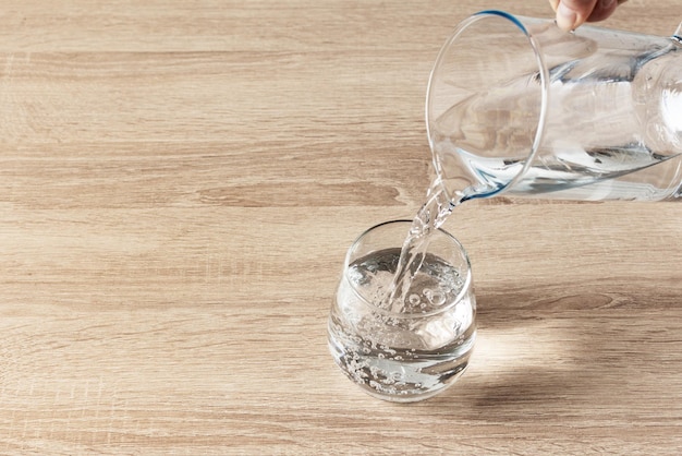 Versare l'acqua da una brocca in un bicchiere su fondo di legno