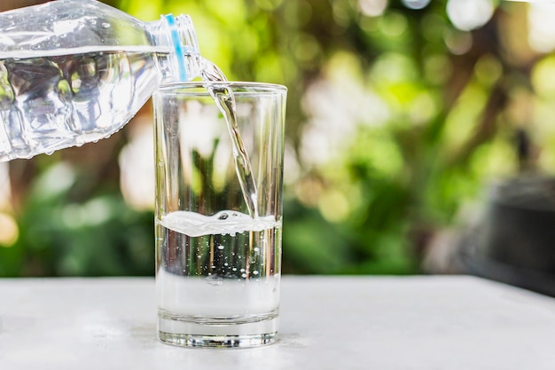 Versare l'acqua dalla bottiglia al bicchiere sullo sfondo della natura bokhe