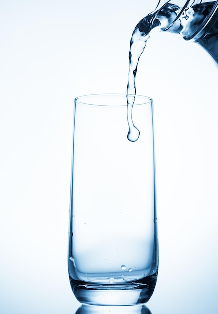 Versare l'acqua dalla brocca di vetro su sfondo blu