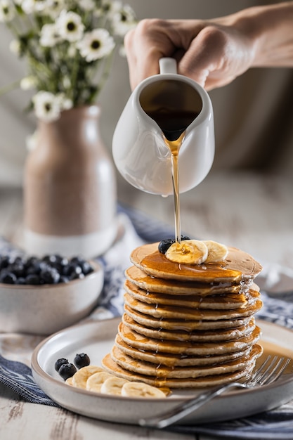 Versare lo sciroppo d'acero su frittelle di banana fatte in casa con mirtilli, ricette facili di cucina casalinga