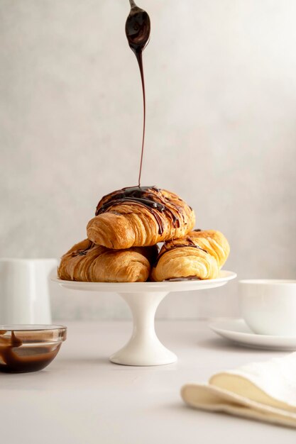 Versare lo sciroppo di cioccolato sui croissant su sfondo luminoso L'ora della colazione