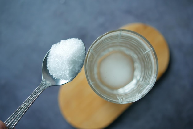 Versare lo zucchero bianco in un bicchiere d'acqua sul tavolo