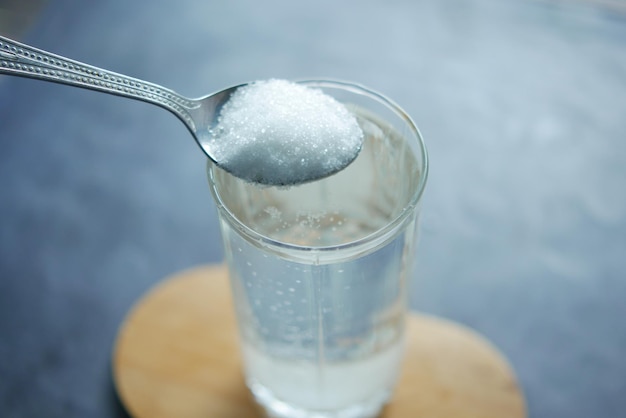 Versare lo zucchero bianco in un bicchiere d'acqua sul tavolo