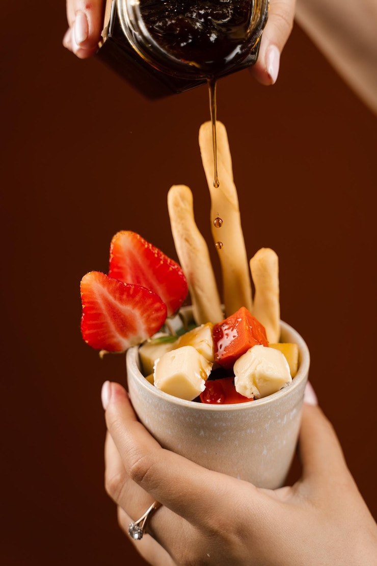 Foto versare marmellata su mix di formaggi bastoncini grissini e fragola in tazza idea creativa per pubblicizzare un negozio di formaggi