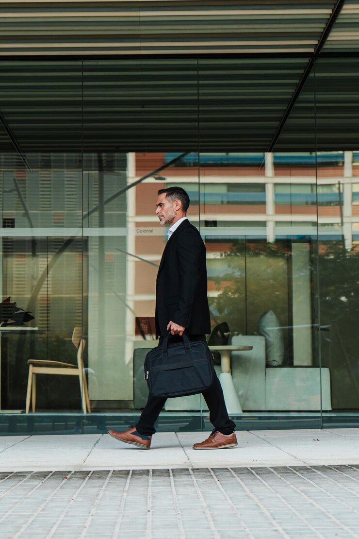 Vertical full length portrait of a mature business man walking and holding a laptop bag mid adult