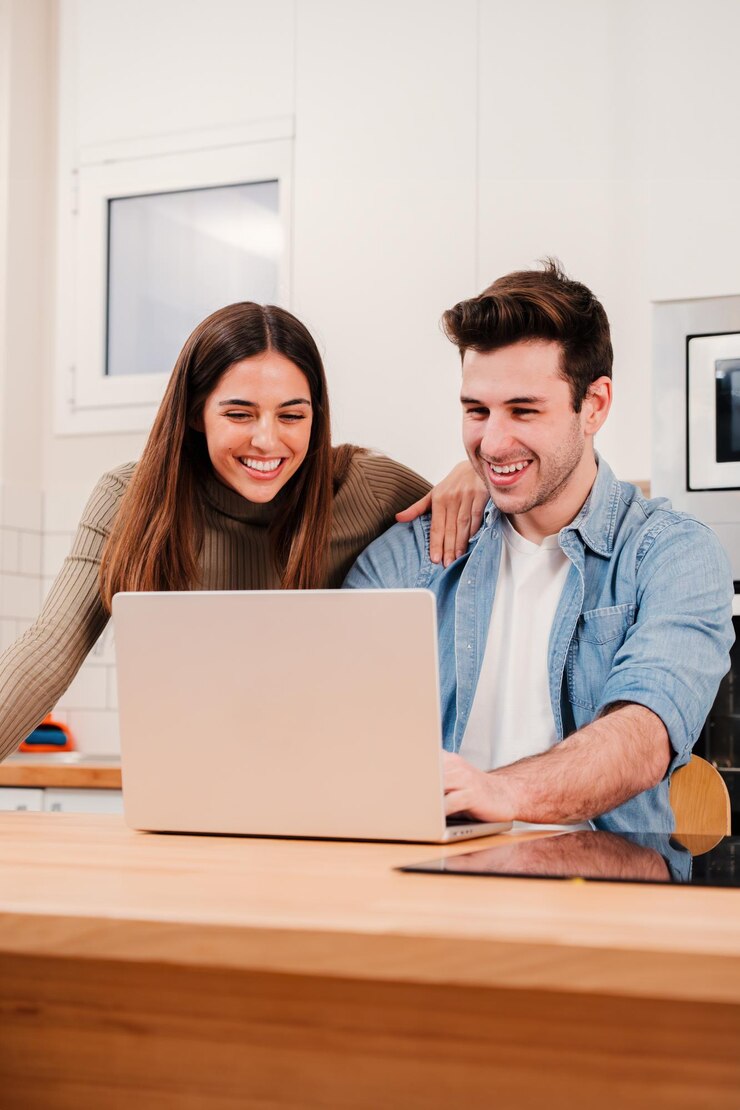 Vertical portrait of young couple browsing on internet at home kitchen using a laptop happy husband