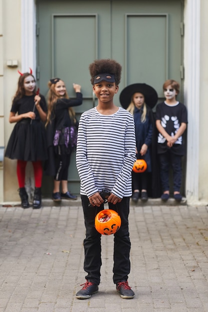 Verticale a figura intera ritratto di multietnico gruppo di bambini che indossano costumi di Halloween mentre dolcetto o scherzetto insieme, concentrarsi sul ragazzo afro-americano in primo piano