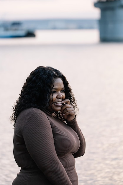 Verticale dai capelli neri sorridente paffuta donna interrazziale afroamericana africana contro il lago o il fiume durante le vacanze estive