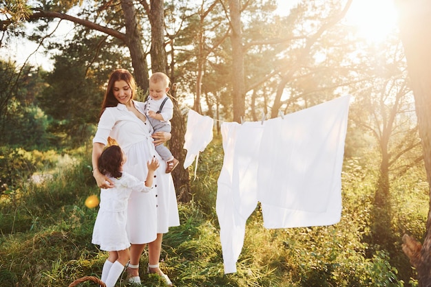 Vestiti bianchi appesi alla corda per asciugare Giovane madre con la sua piccola figlia e figlio è all'aperto nella foresta Bel sole