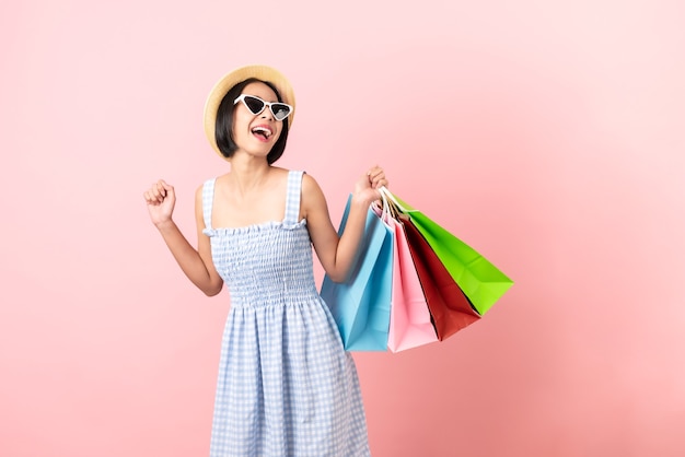 Vestiti casual della giovane donna asiatica sorridente che tengono i multi sacchetti della spesa colorati su fondo rosa-chiaro.