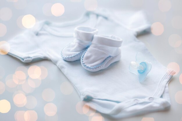 vestiti per bambini, infanzia, maternità e concetto di oggetto - primo piano di body bianco, stivaletti e succhietto per neonato sul tavolo