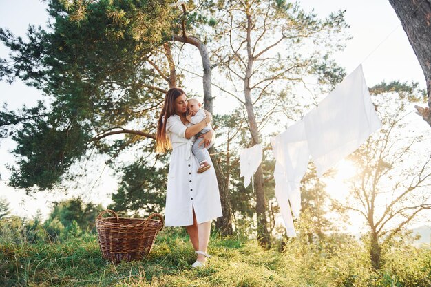 Vestiti puliti appesi alla corda per asciugare Giovane madre con il figlio piccolo è all'aperto nella foresta Bel sole