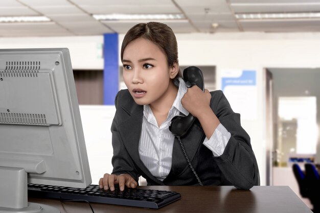 Vestito d&#39;uso asiatico confuso della donna di affari che guarda lo schermo mentre tenendo telefono