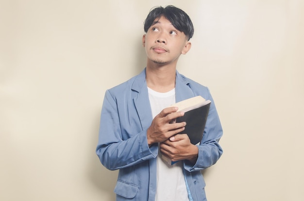 Vestito da portare del college del giovane uomo asiatico con il libro della holding di espressione di pensiero