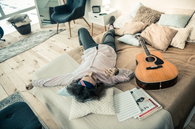 Vestito elegante. Un bell'uomo stanco che si rilassa sul letto coperto circondato da cuscini e album per appunti