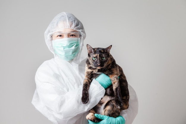 Vet sorridente felice mentre gioca con un gatto. medico veterinario in tuta protettiva DPI in possesso di un adorabile gatto presso la clinica degli animali. Assistenza sanitaria Pet e prevenzione Strategia COVID-19 Concetto di coronavirus