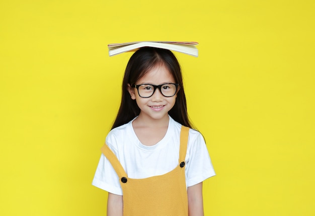 Vetri da portare della ragazza del bambino con il libro sulla testa su priorità bassa gialla