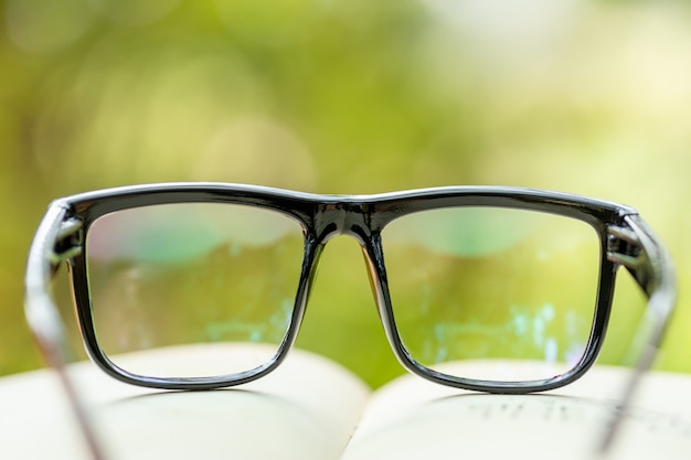 Vetri dell'occhio e del libro sulla tavola di legno con il concetto verde astratto della lettura e di istruzione della sfuocatura della natura