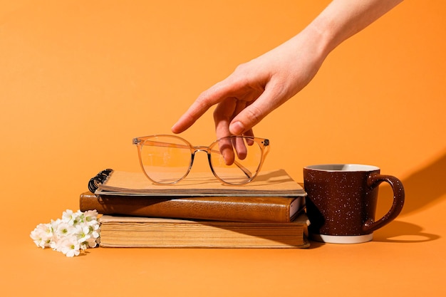 Vetri sulla tazza dei libri e sulla mano femminile su fondo giallo