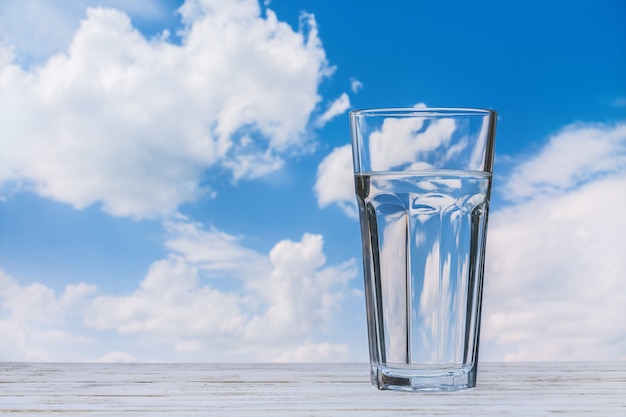 Vetro con acqua sulla tavola di legno. Cielo azzurro con nuvole bianche. Copia spazio.