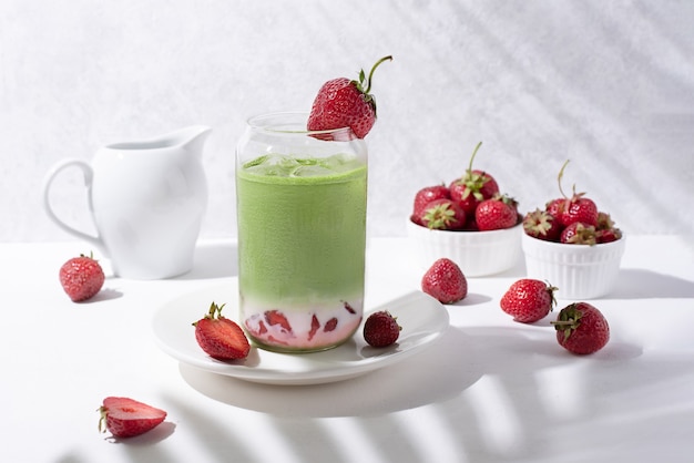 Vetro con latte matcha alla fragola con fragole su sfondo bianco con belle ombre dai rami, primo piano.